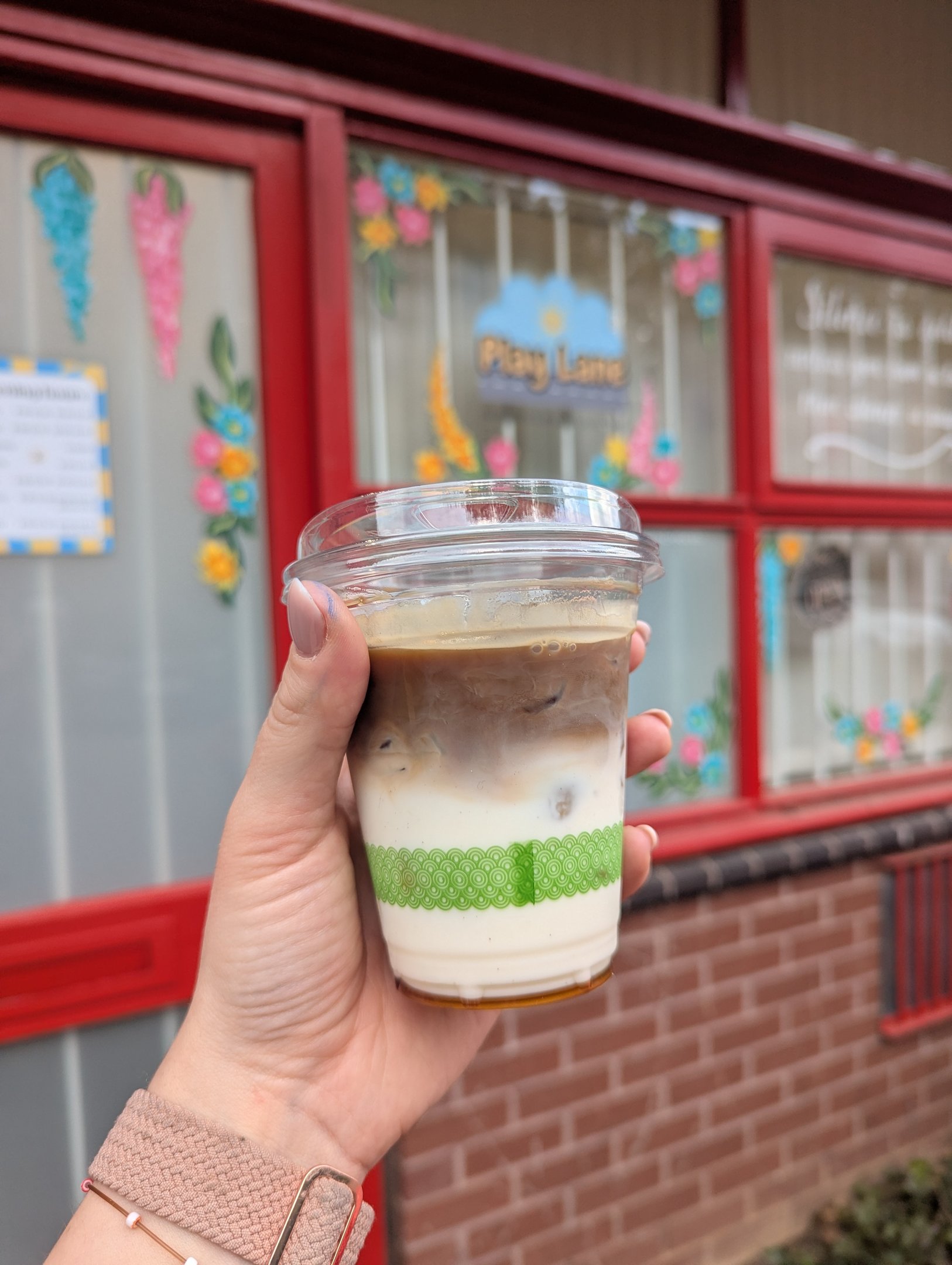 An iced coffee held up outside the Play Lane window