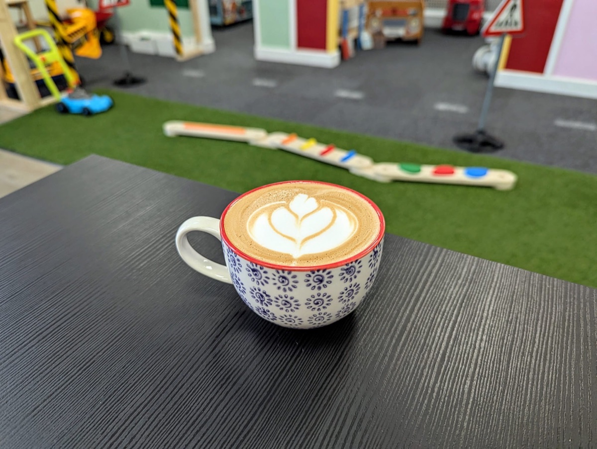 An iced coffee held up outside the Play Lane window